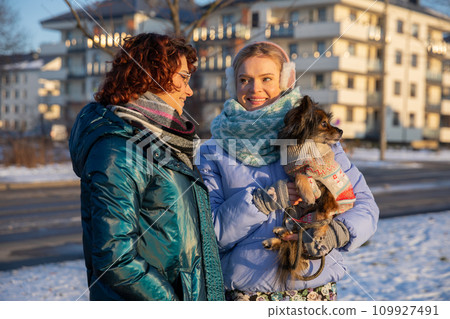 A woman holds her dog in her arms during a winter walk. A woman holds her dog in her arms during a winter walk. 109927491
