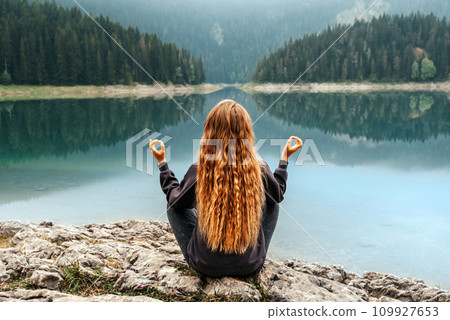 Woman Meditating in Yoga Pose by Mountain Lake 109927653
