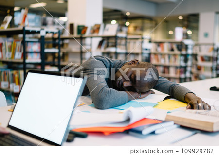 Tired ethnic student falling asleep in library Tired ethnic student falling asleep in library 109929782