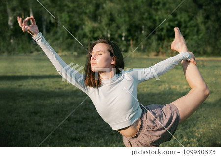 Adult female practising yoga outside, Dancer Pose Adult female practising yoga outside, Dancer Pose 109930373