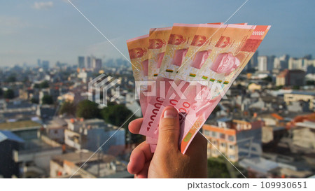 Man's Hand holding rupiah money against the backdrop of the city of Jakarta. 109930651