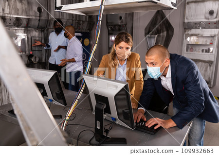 Man and woman in protective masks in panic looking for a solution on the computer in quest room 109932663