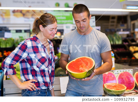 Positive couple choosing watermelon in fruit and vegetable section of supermarket Positive couple choosing watermelon in fruit and vegetable section of supermarket 109932795