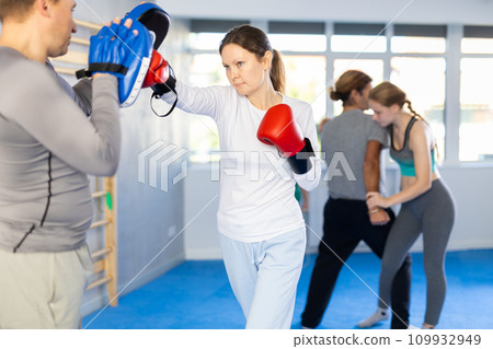 Woman works out strength and speed of boxing punch mitts with help of partner in boxing paws Woman works out strength and speed of boxing punch mitts with help of partner in boxing paws 109932949