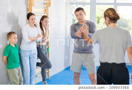 Man coach shows family students technique of performing painful modus with help of wringing hand 109933368