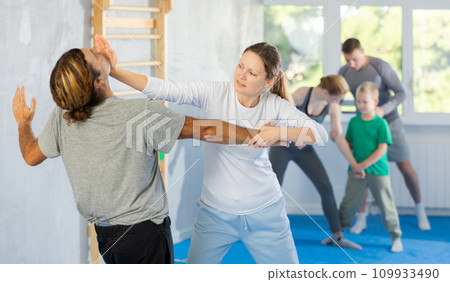 Woman and man in group self-defense classes practicing sparring technique of blowing to chin in gym Woman and man in group self-defense classes practicing sparring technique of blowing to chin in gym 109933490