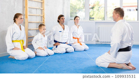 Family of athletes sit in row in front of man coach and listen attentively. 109933531