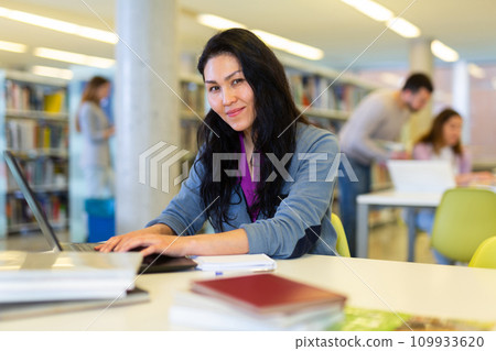 Asian woman using laptop and books for research in library 109933620