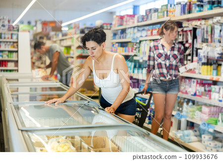 Woman standing at refrigerator in supermarket, choosing frozen food 109933676
