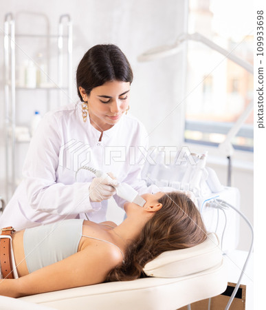 Female cosmetologist performing facial skin cleansing with ultrasonic shovel on woman 109933698
