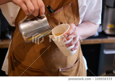 The coffee machine is frothing milk. Barista's hands hold a jug of milk. The coffee machine is frothing milk. Barista's hands hold a jug of milk. 109936355