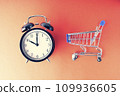 An empty shopping cart and an alarm clock on a red scarlet background. Shopping, online shopping concept, time to buy concept, copy space, top view, 109936605