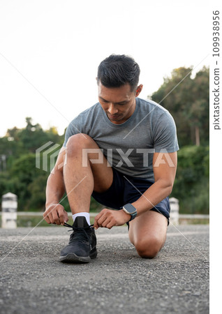 A strong, fit Asian man in sportswear is tying his shoelaces and getting ready before exercising. A strong, fit Asian man in sportswear is tying his shoelaces and getting ready before exercising. 109938956