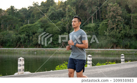 A handsome, focused Asian man in sportswear is running outdoors in the morning. A handsome, focused Asian man in sportswear is running outdoors in the morning. 109938983