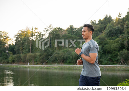 A handsome, focused Asian man in sportswear is running outdoors in the morning. A handsome, focused Asian man in sportswear is running outdoors in the morning. 109938984