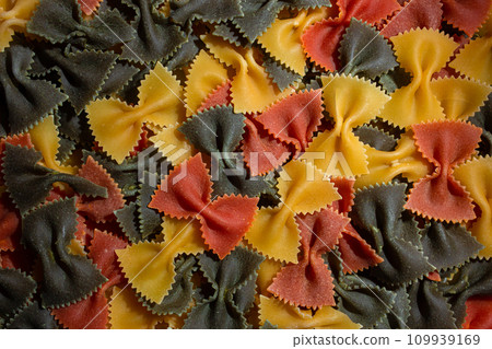 Dry Uncooked Colored Farfalle Pasta and Raw Macaroni on a Textured Background Dry Uncooked Colored Farfalle Pasta and Raw Macaroni on a Textured Background 109939169