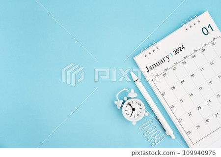 January 2024, Monthly desk calendar for 2024 year and alarm clock with paper clips on blue color background. January 2024, Monthly desk calendar for 2024 year and alarm clock with paper clips on blue color background. 109940976