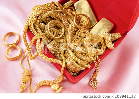 Many gold necklaces and gold bars in red box on velvet cloth. 109941138