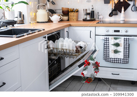 A lot of dirty dishes in the dishwasher in the festive kitchen. Helping the hostess, economy and ecology. Cleaning in the kitchen for the holidays of Christmas and New Year, after the feast and guests A lot of dirty dishes in the dishwasher in the festive kitchen. Helping the hostess, economy and ecology. Cleaning in the kitchen for the holidays of Christmas and New Year, after the feast and guests 109941300