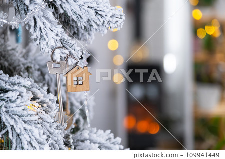 Key to the house with a keychain is hanging on the Christmas tree. A gift for New Year, Christmas. Building, design, project, moving to new house, mortgage, rent and purchase real estate. Copy space 109941449