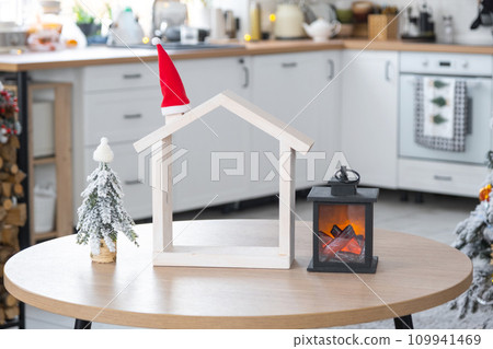 Cozy Christmas decor tiny house of small size on table of festive white modern kitchen. Gift for New Year. Insurance, moving to new house, mortgage, rent and purchase real estate Cozy Christmas decor tiny house of small size on table of festive white modern kitchen. Gift for New Year. Insurance, moving to new house, mortgage, rent and purchase real estate 109941469