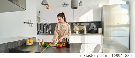 Portrait of beautiful brunette girl chopping vegetables for meal, making salad in the kitchen, eating healthy food, preparing dinner 109941886