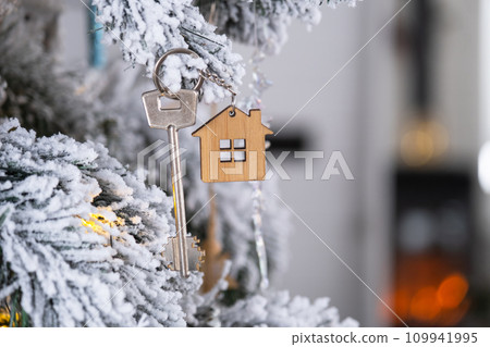 Key to the house with a keychain is hanging on the Christmas tree. A gift for New Year, Christmas. Building, design, project, moving to new house, mortgage, rent and purchase real estate. Copy space Key to the house with a keychain is hanging on the Christmas tree. A gift for New Year, Christmas. Building, design, project, moving to new house, mortgage, rent and purchase real estate. Copy space 109941995