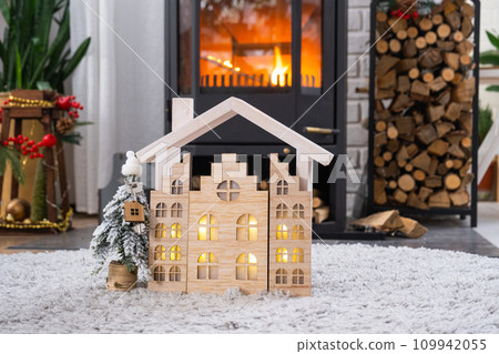Key on Christmas tree and tiny house on cozy home with Christmas decor near the burning stove fireplace. Gift for New Year. Insurance, moving to new house, mortgage, rent and real estate 109942055