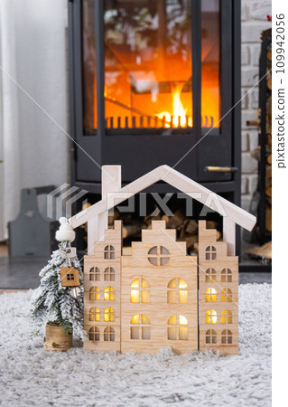 Key on Christmas tree and tiny house on cozy home with Christmas decor near the burning stove fireplace. Gift for New Year. Insurance, moving to new house, mortgage, rent and real estate 109942056