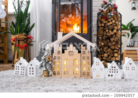 Key on Christmas tree and tiny house on cozy home with Christmas decor near the burning stove fireplace. Gift for New Year. Insurance, moving to new house, mortgage, rent and real estate 109942057