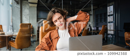 Portrait of woman feels pain in neck, sits in office with laptop, has tension in muscles after working all day Portrait of woman feels pain in neck, sits in office with laptop, has tension in muscles after working all day 109942388