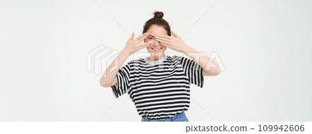 Portrait of girl waiting for surprise, covers eyes with hands, peeking through fingers, stands over white background Portrait of girl waiting for surprise, covers eyes with hands, peeking through fingers, stands over white background 109942606