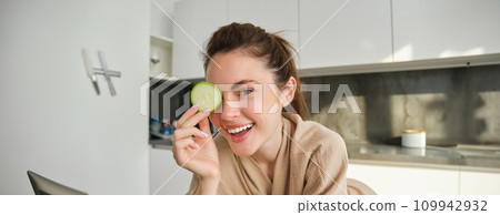 Portrait of happy, smiling young woman in the kitchen, cooking, chopping zucchini, holding vegetables and looking happy, preparing vegan food meal at home Portrait of happy, smiling young woman in the kitchen, cooking, chopping zucchini, holding vegetables and looking happy, preparing vegan food meal at home 109942932