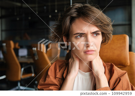 Portrait of woman feels pain in neck, sits in office with laptop, has tension in muscles after working all day 109942959