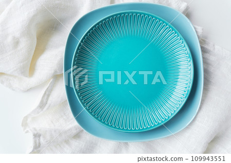 A vibrant blue plate on a white cloth. The cloth underneath is textured and appears soft and delicate. There s a contrast between the bold color of the plate and the neutral tone of the cloth. 109943551