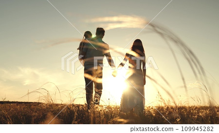 Silhouettes of parents walk holding hands with daughter sitting in arms of father 109945282