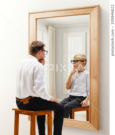 Man in formal wear sitting and looking in mirror with reflection of him being a child. Dreams and reality. Conceptual collage. Age, past and present, generation Man in formal wear sitting and looking in mirror with reflection of him being a child. Dreams and reality. Conceptual collage. Age, past and present, generation 109946621