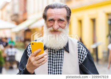 Elderly man use smartphone typing text messages browsing internet finishing work looking at camera 109947819
