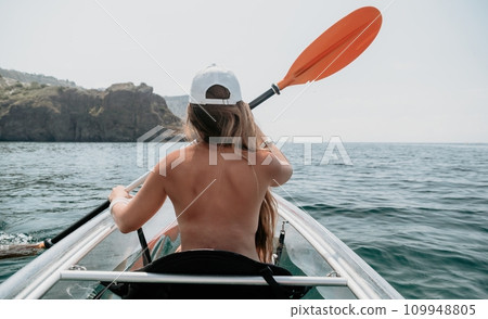 Woman in kayak back view. Happy young woman with long hair floating in transparent kayak on the crystal clear sea. Summer holiday vacation and cheerful female people relaxing having fun on the boat 109948805