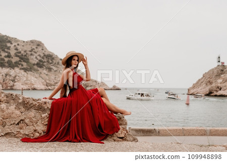 Woman travel portrait. Happy woman with long hair looking at camera and smiling. Close up portrait cute woman in a res long dress posing on backdrop of old travel city near sea 109948898