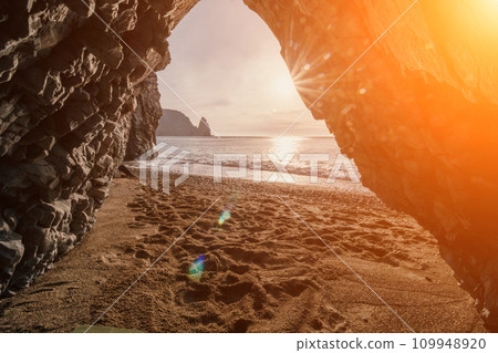sunset seascape, captured from a rocky volcanic cave, view of the beach, sand, pebbles, and volcanic basalt formations, illuminated by the warm glow of the sun. sunset seascape, captured from a rocky volcanic cave, view of the beach, sand, pebbles, and volcanic basalt formations, illuminated by the warm glow of the sun. 109948920