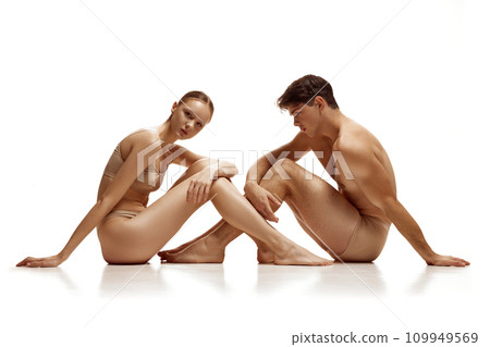 Full length portrait of beautiful couple, man and woman with prefect body shapes sitting on floor and posing against white studio background. Full length portrait of beautiful couple, man and woman with prefect body shapes sitting on floor and posing against white studio background. 109949569