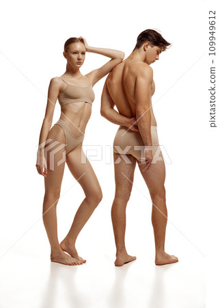 Body size portrait of naked couple, woman and man with perfect athletic bodies posing in beige underwear against white studio background. 109949612