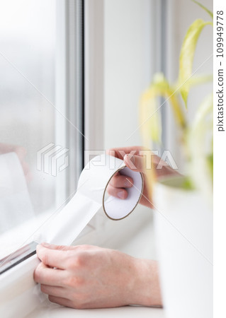 Mans hands putting draught excluder tape on the window. 109949778