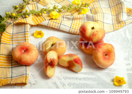 Halves and several whole saturn peaches or flat peach on white wooden background.. Halves and several whole saturn peaches or flat peach on white wooden background.. 109949793