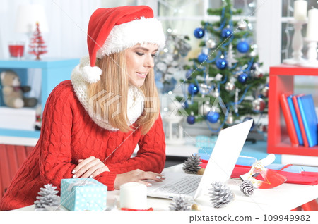 Happy young woman using laptop preparing for Christmas Happy young woman using laptop preparing for Christmas 109949982