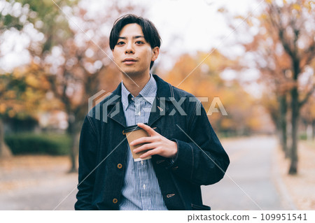 一名男子一邊喝著咖啡，一邊沿著種滿秋葉的大道散步 109951541