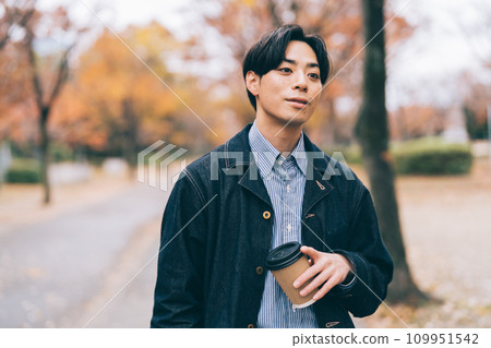 一名男子一邊喝著咖啡，一邊沿著種滿秋葉的大道散步 109951542