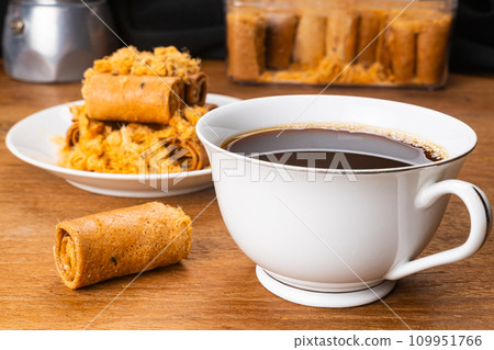 Cup of hot black coffee with a pile of dried shrodded pork crispy coconut roll. 109951766