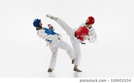 Two men in kimono and helmets practicing taekwondo, training, fighting isolated over white background. Martial arts, combat sport Two men in kimono and helmets practicing taekwondo, training, fighting isolated over white background. Martial arts, combat sport 109952834
